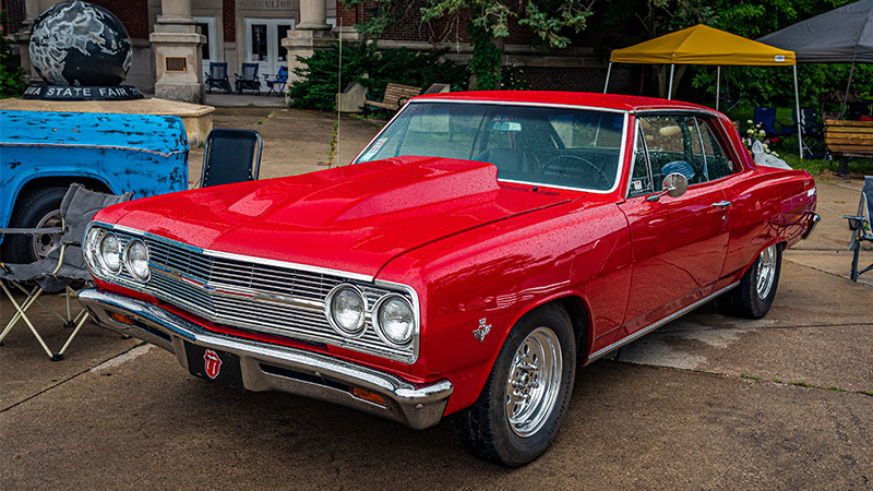 A red 1965 Chevy Chevelle parked in a lot at a car show