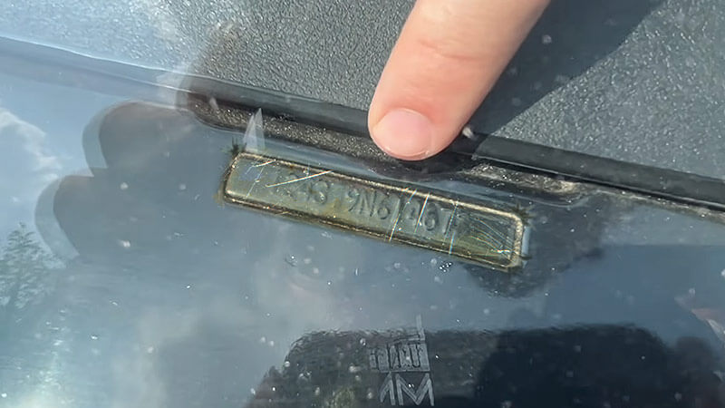 A close up of a scratched up VIN plate with a man's finger pointing at it