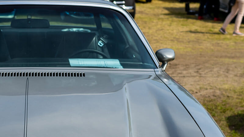 A zoomed-in picture of a silver 1970-1981 Chevy Camaro with an emphasis on the hood and windshield of the car