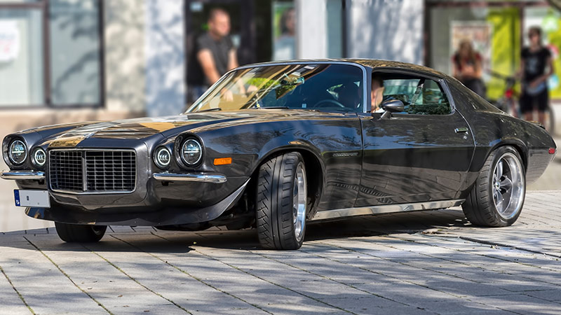A black classic Chevy Camaro parked in a parking lot in front of a building