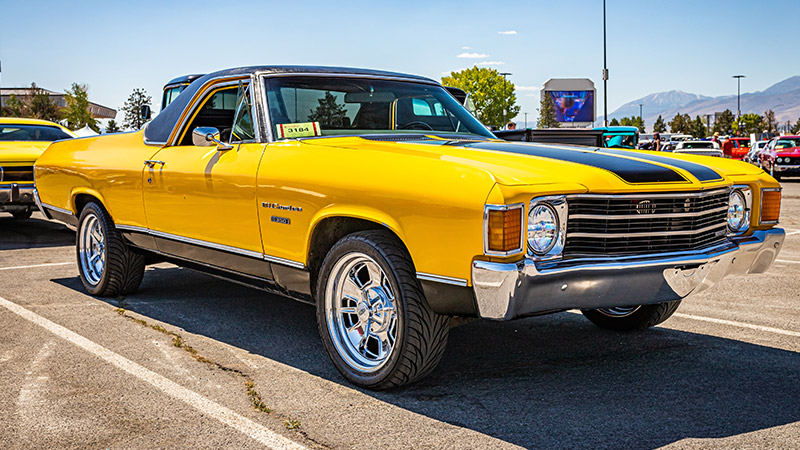 A wide angle shot of a yellow 1972 Chevy El Camino with black racing stripes parked in a parking lot