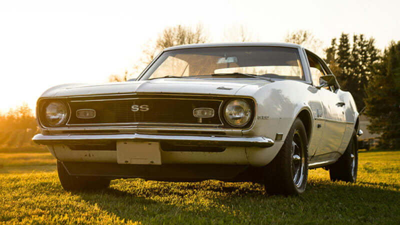A white 1968 Chevy Camaro parked in a field during sunset